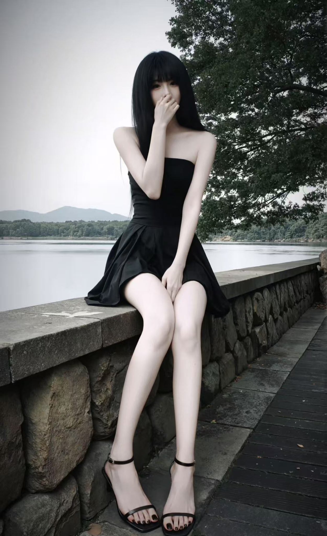 一位穿着黑色衣服的女人坐在湖边的墙上。