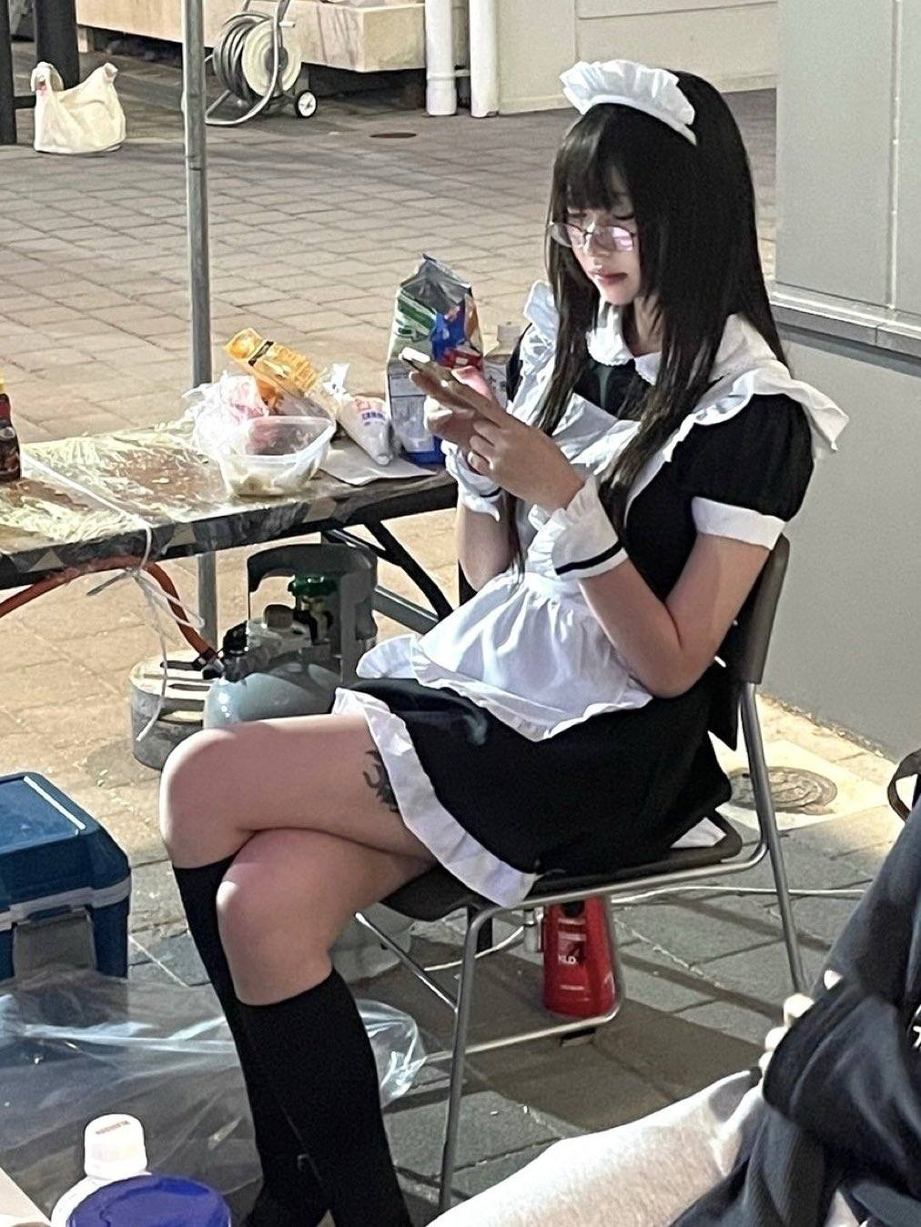 穿着女仆服的女人坐在一张桌子上,看着她的手机。
