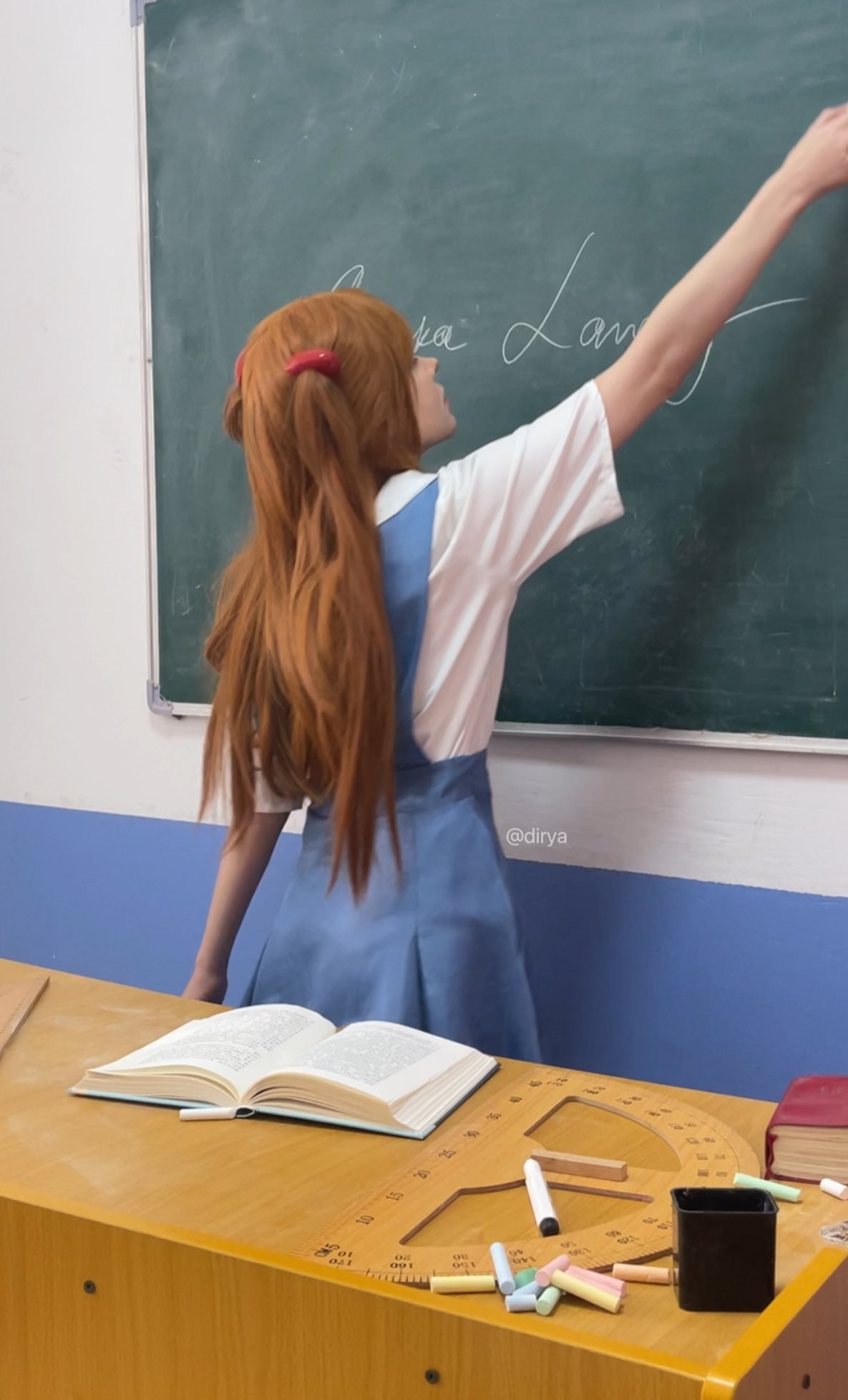 一位穿着一只马尾巴和一件蓝色的裙子的女孩站在板前面。