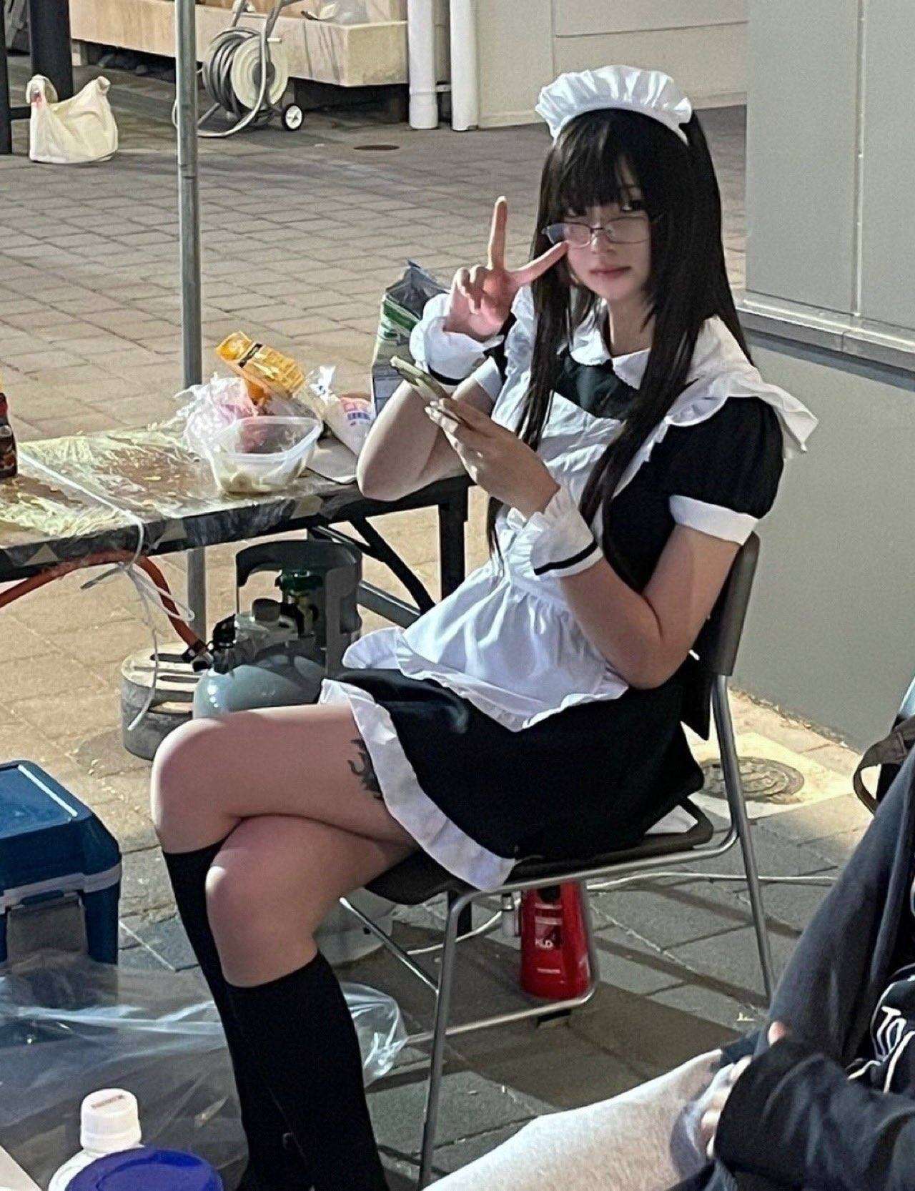 穿着女仆服的女人坐在一张桌子上,看着她的手机。