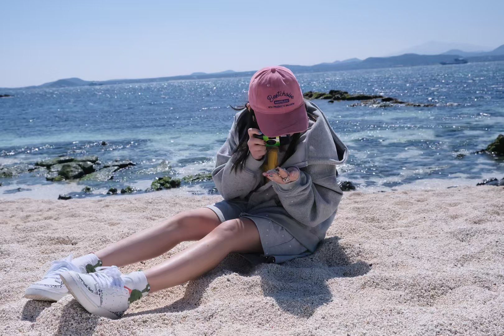 穿着粉红色的帽子和太阳镜的女人站在一个岩石海滩上。