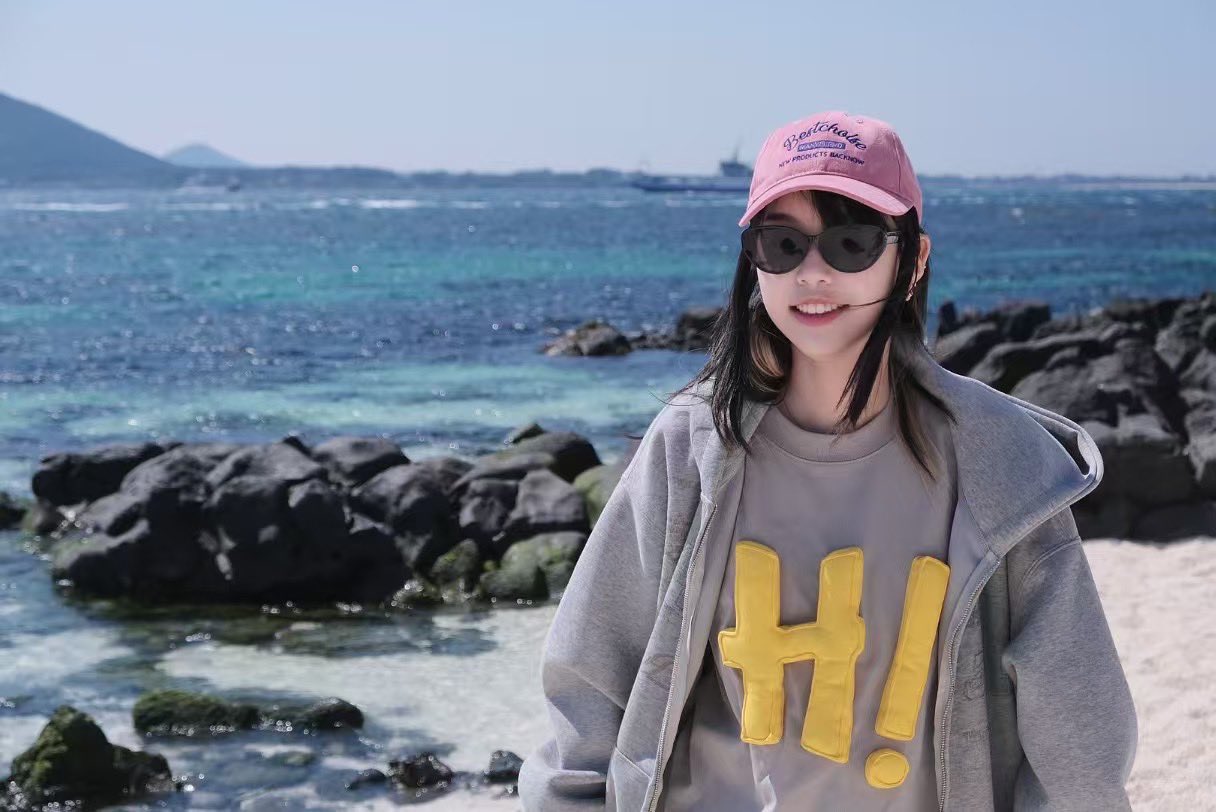 穿着粉红色的帽子和太阳镜的女人站在一个岩石海滩上。