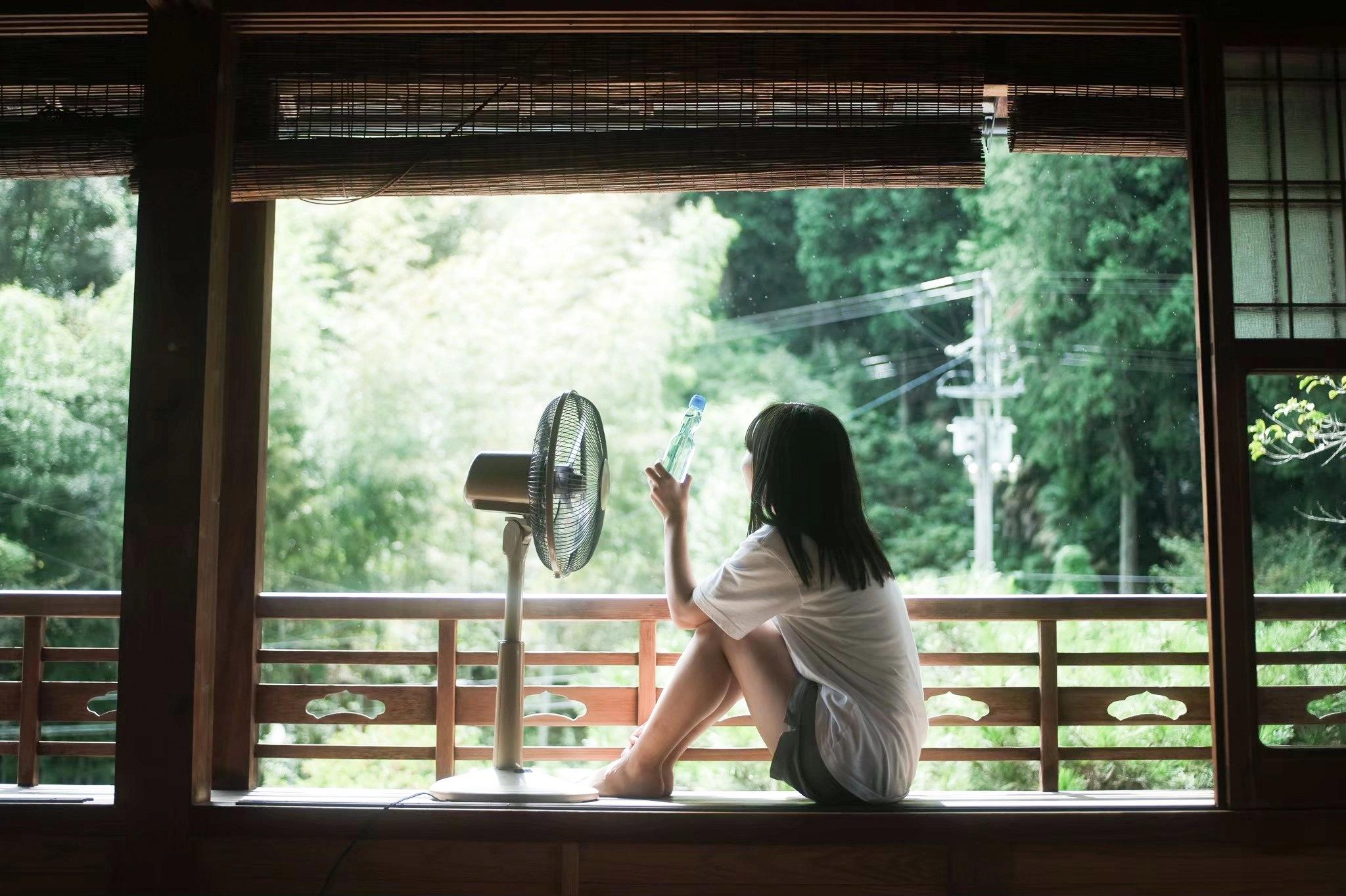 女孩坐在窗户上,拿着一个风扇和一瓶。