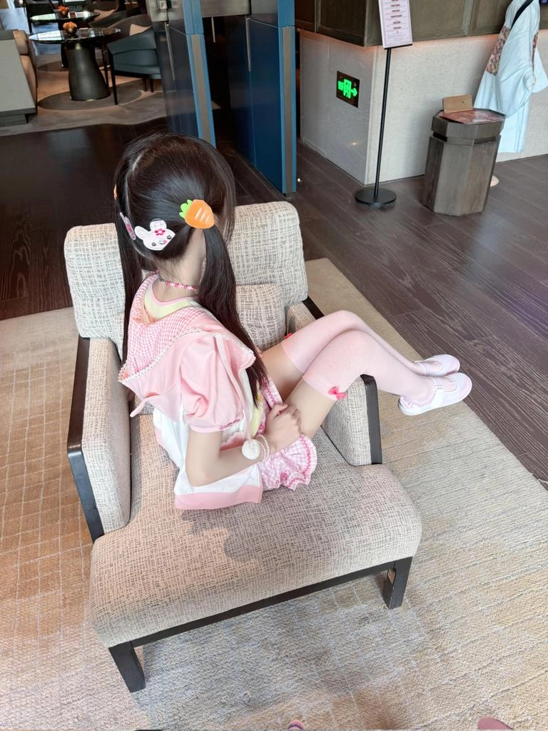 穿着粉红色的裙子和白色袜子的女孩坐在椅子上。