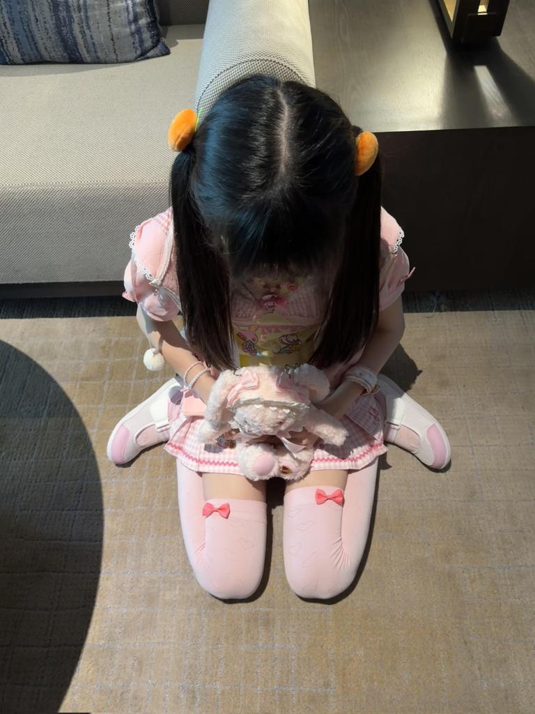 穿着粉红色的裙子和白色袜子的女孩坐在椅子上。