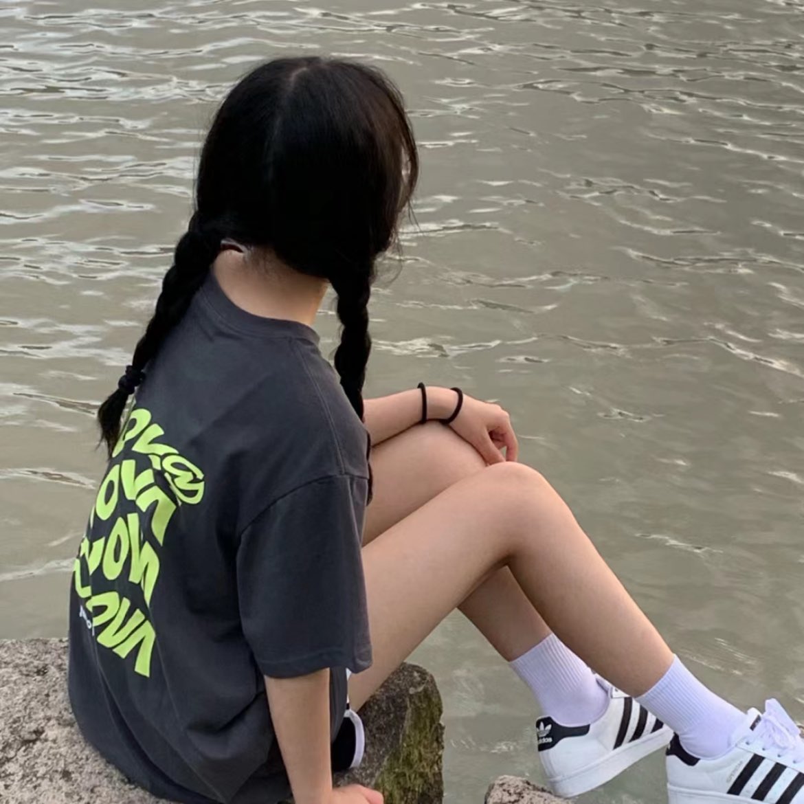 一位戴着眼镜和灰色衬衫的女人坐在水边的岩石上。