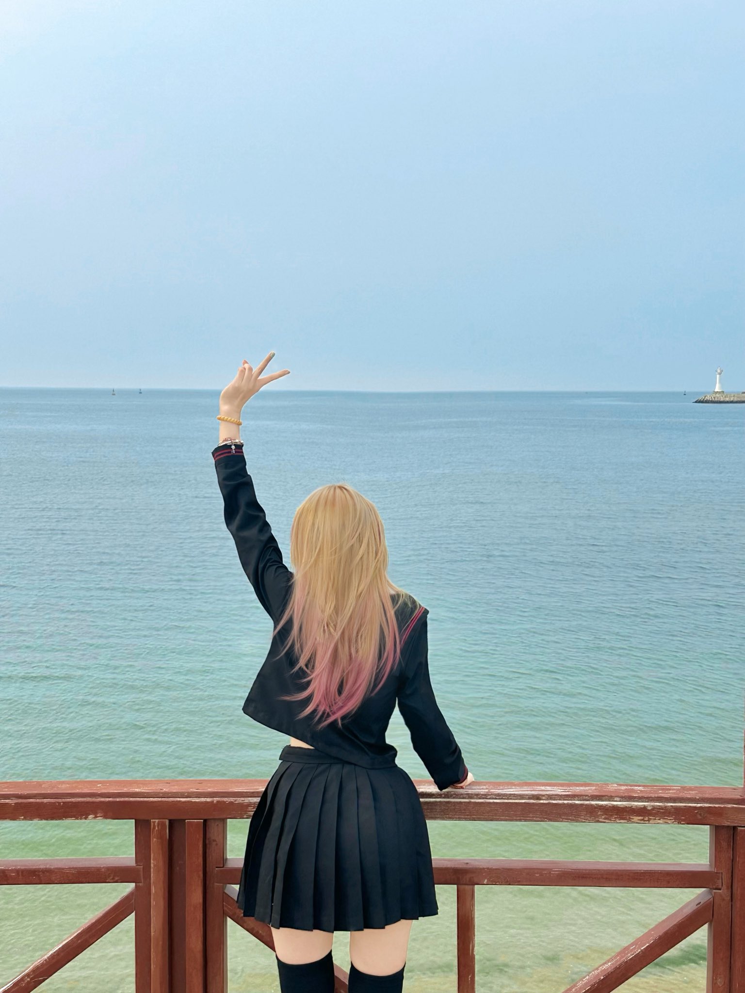 粉红色的头发和黑色夹克的女人在海洋上做和平的信号。