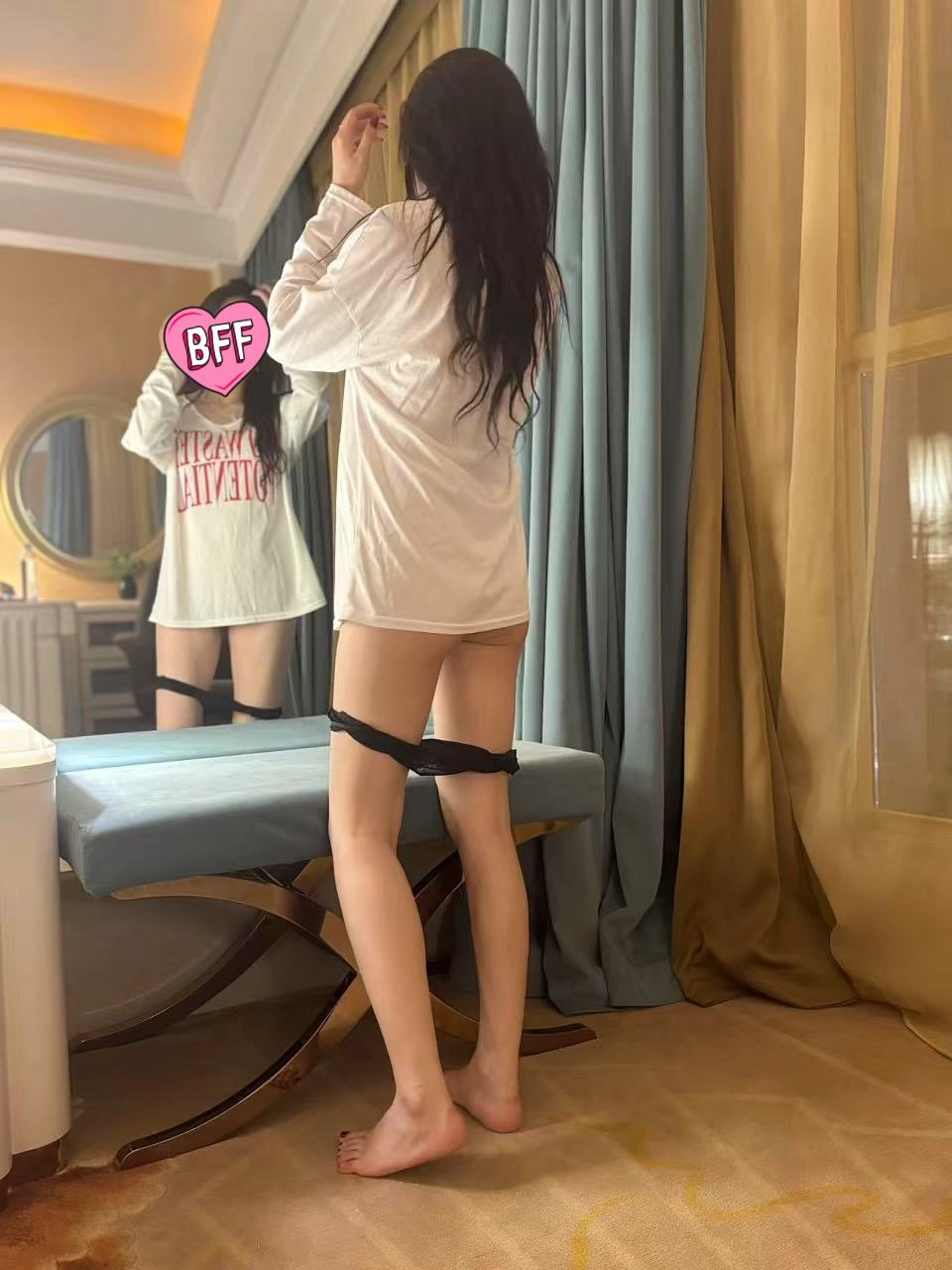 一位穿着白色衬衫和黑色内衣的女人站在镜子前。