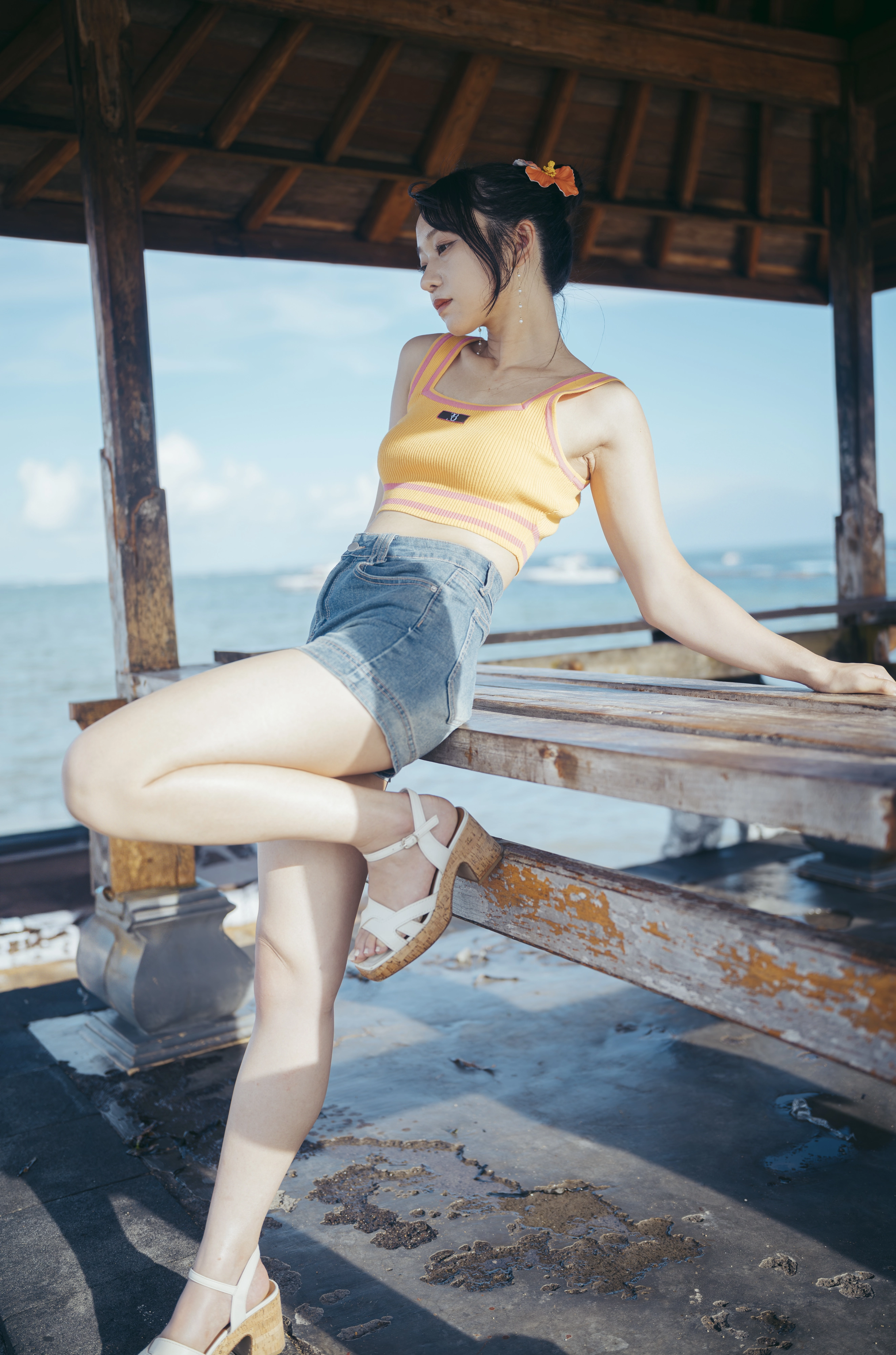 穿着黄色顶部和蓝色短裤的女人坐在一个凳子上。