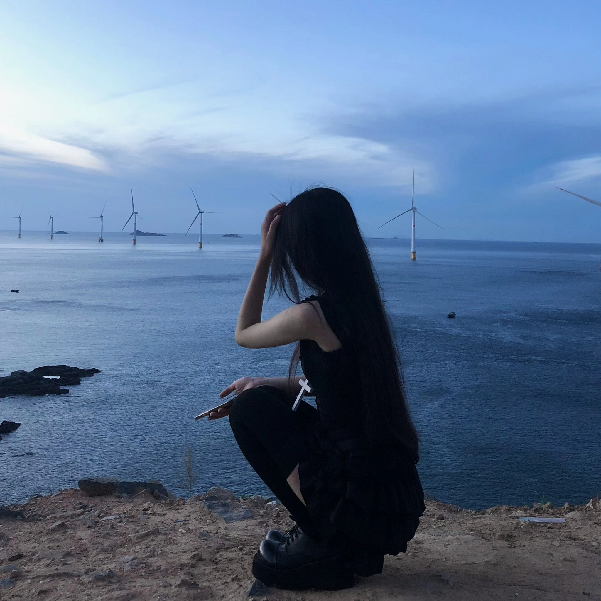 长头发的女人坐在一座俯瞰大海的山上。