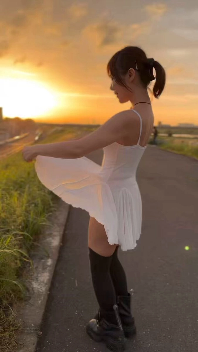 一位穿着白色裙子和黑色靴子的女人站在街上。