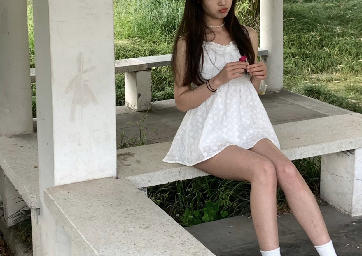 女孩坐在一个凳子上,手里有一朵粉红色的玫瑰。