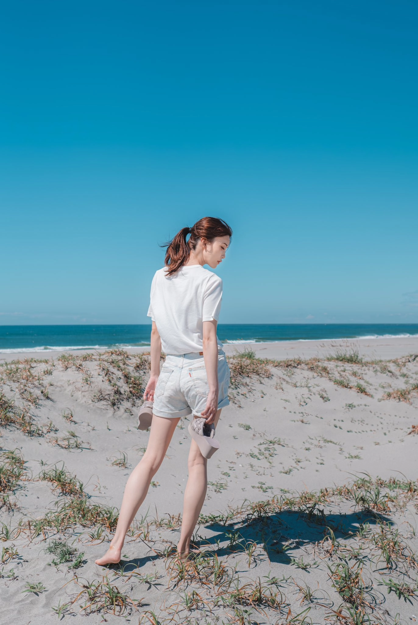 穿着白色衬衫和短裤的女人在海滩上散步。