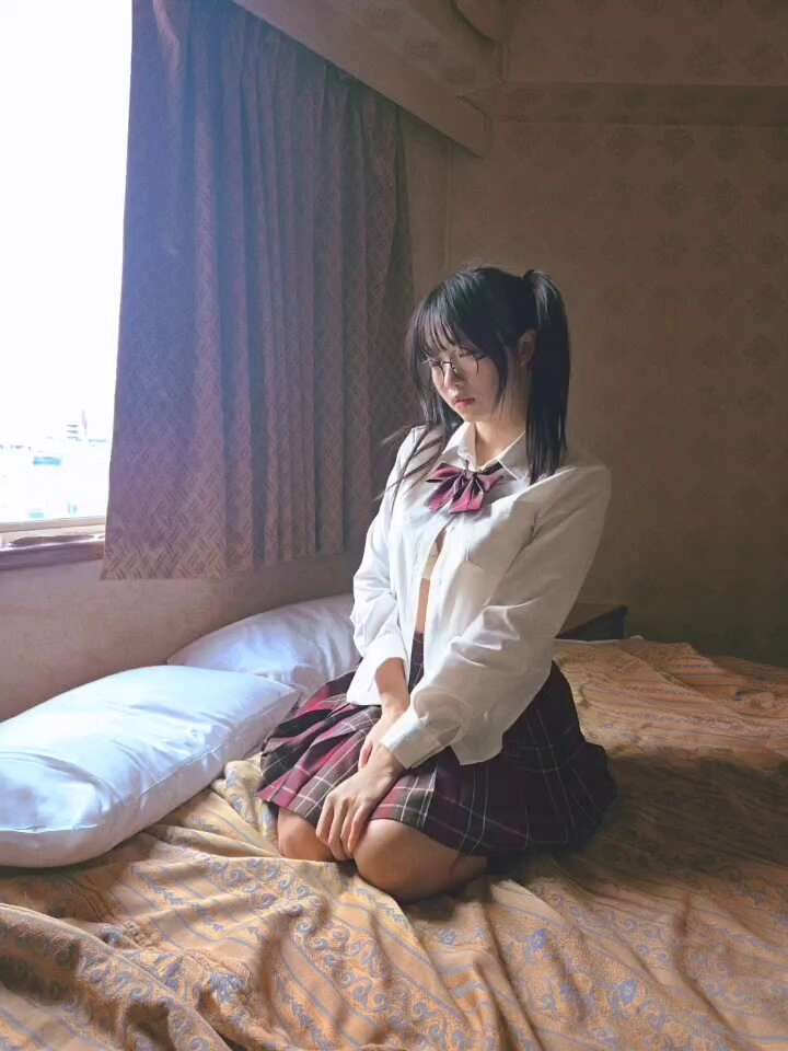 穿着白色衬衫和红色弓的女孩坐在床上。