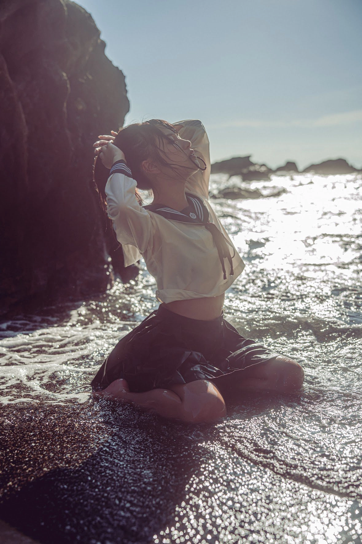 穿着白色衬衫和黑色裙子的女人坐在海滩上。