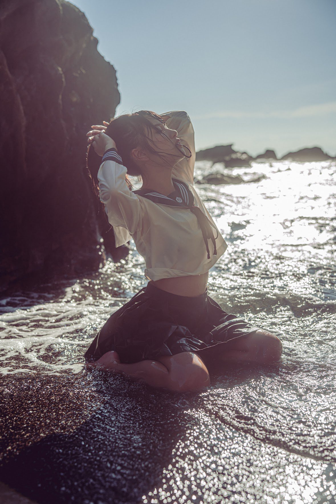 穿着白色衬衫和黑色裙子的女人坐在海滩上。