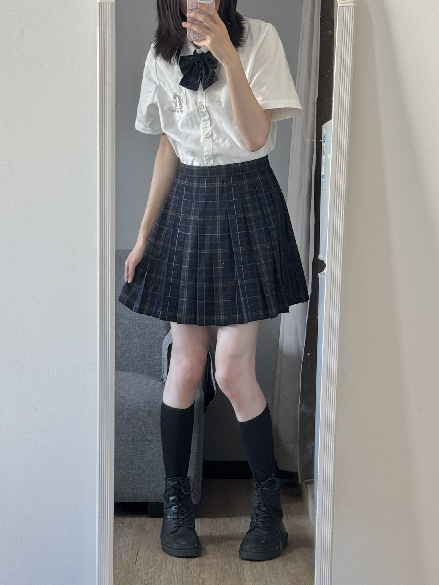 一位穿着一件白色衬衫和一件白色裙子的女人在镜子前拍了一张自拍。