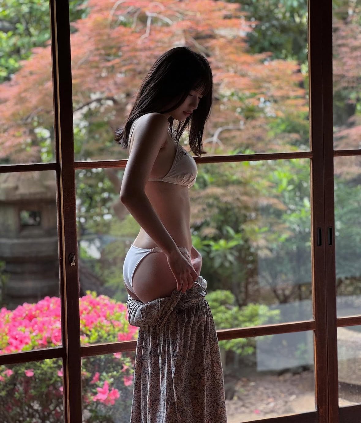 一位穿着白色比基尼顶和鲜花的裙子的女人站在窗前。