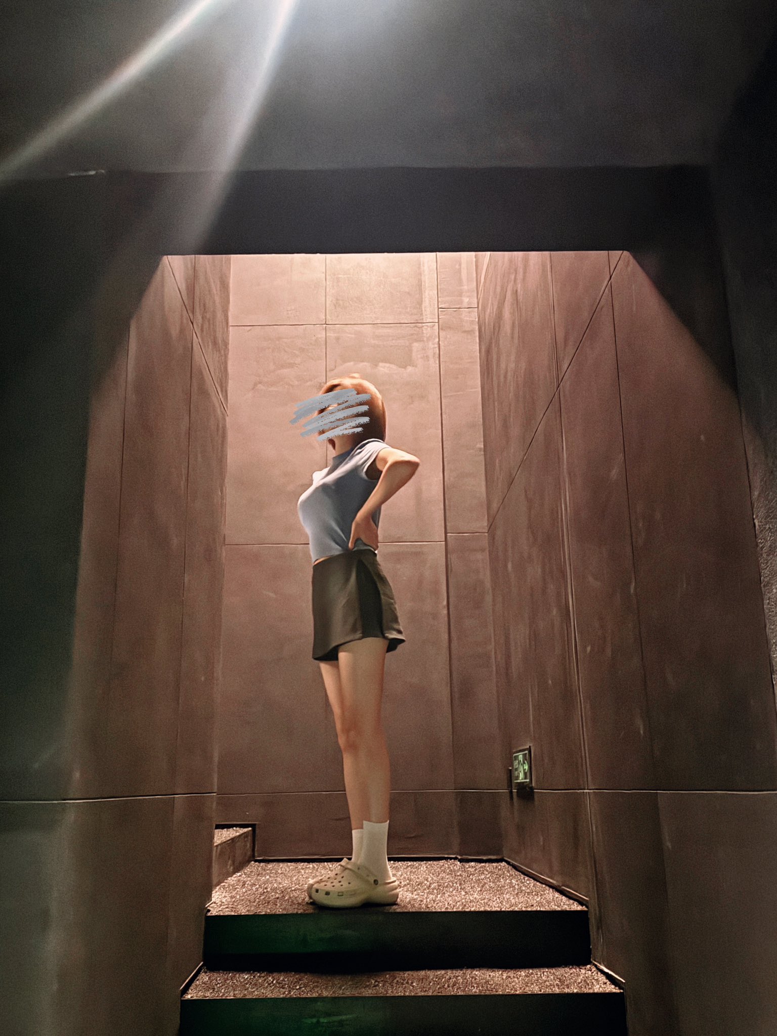 一位穿着蓝色衬衫和黑色短裤的女人站在黑暗的房间里。