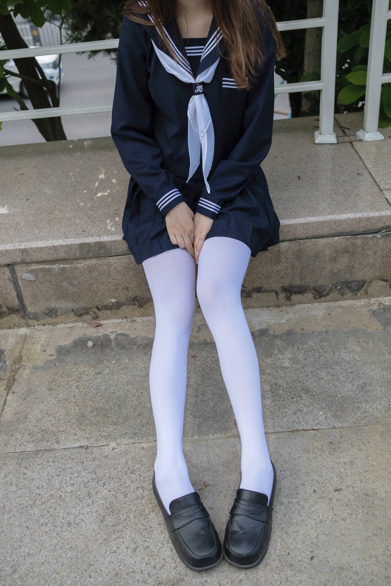 穿着蓝色裙子和白色袜子的女孩坐在一个步骤上。