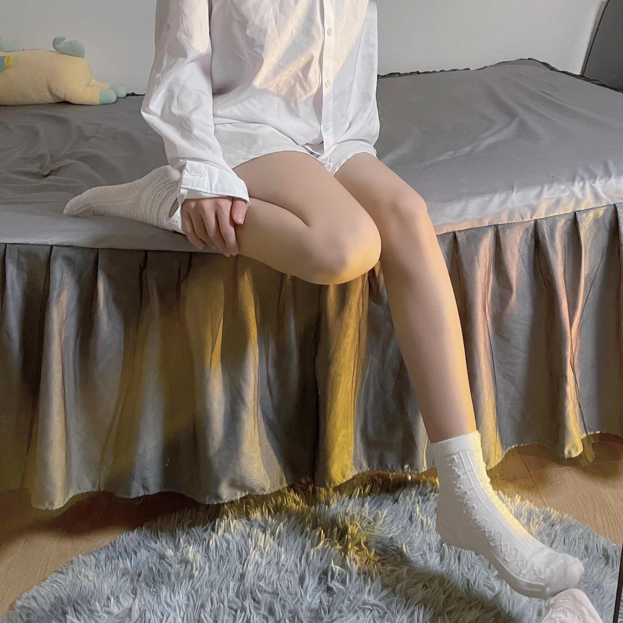 女人坐在床上,身着白色衬衫和白袜子。