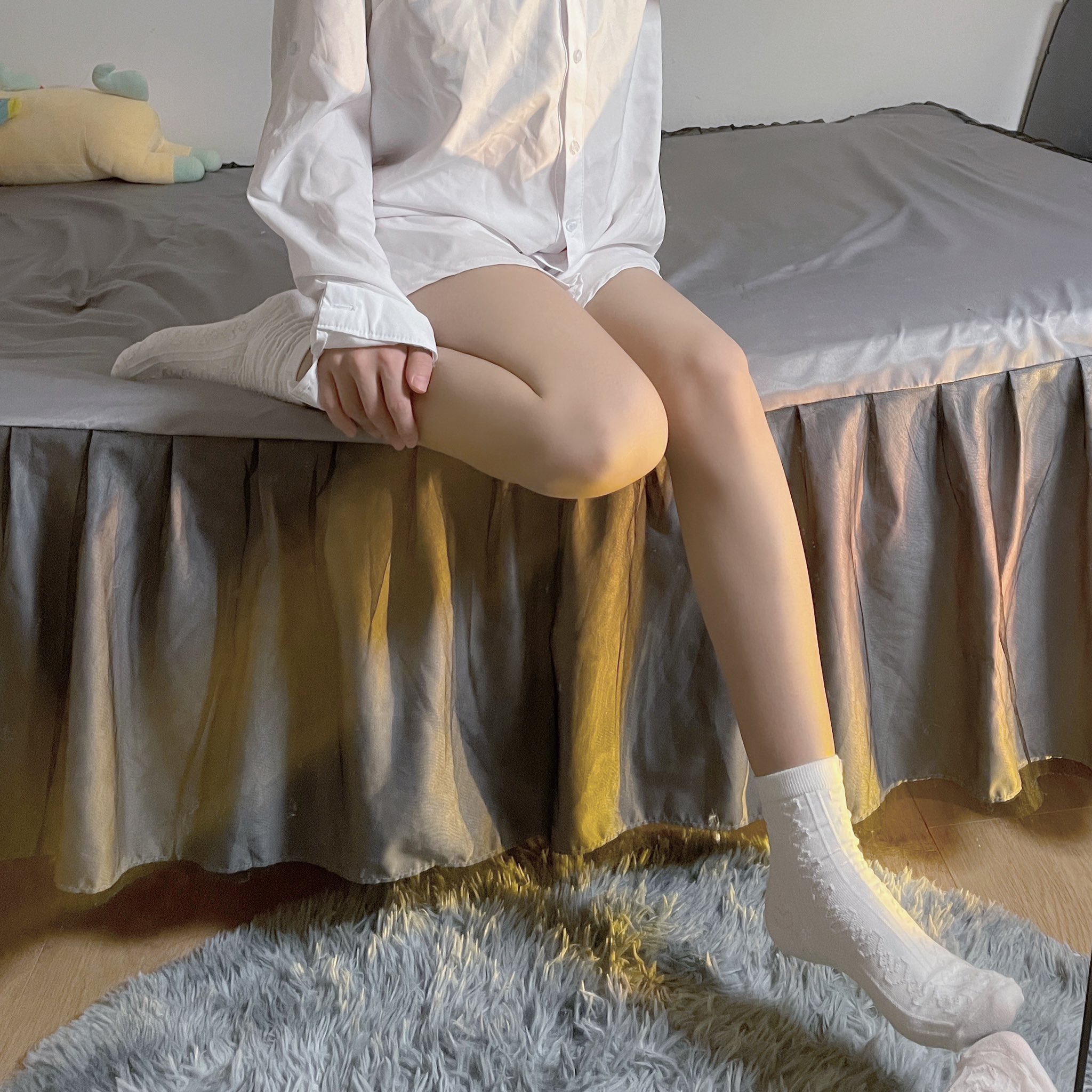 女人坐在床上,身着白色衬衫和白袜子。