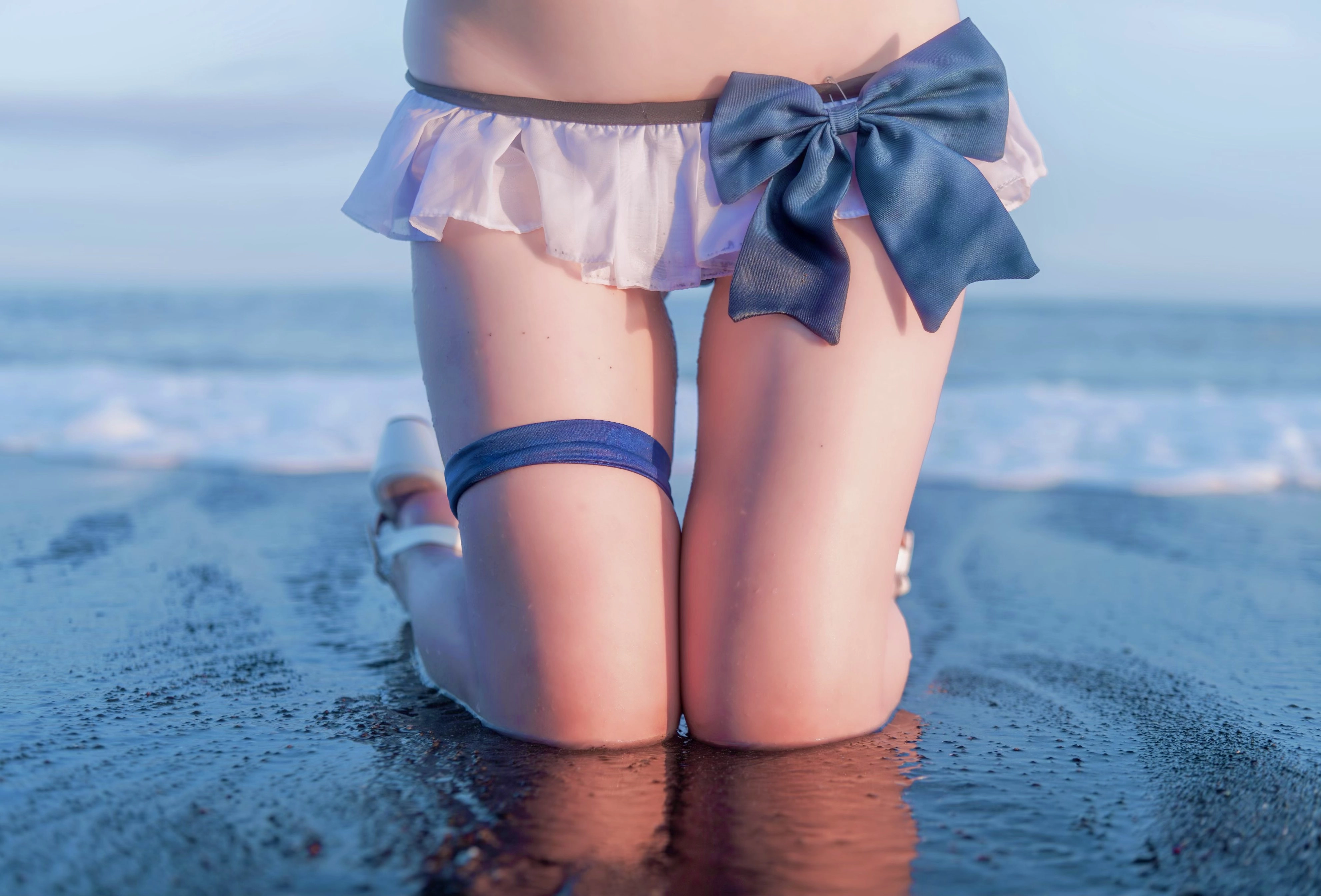 穿着白色裙子和蓝色弓的女人坐在海滩上。