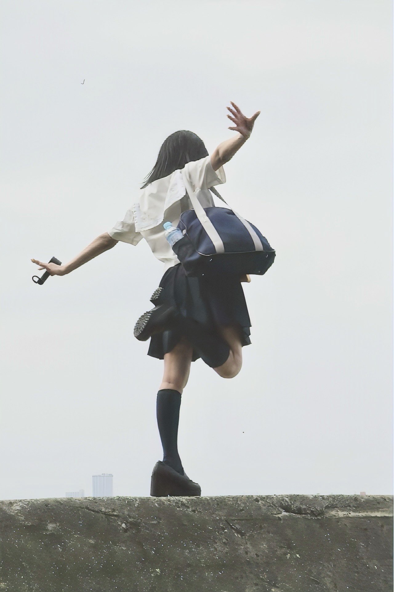 一位穿着白色衬衫和黑色衬衫的女人带着蓝色袋子在空中跳跃。