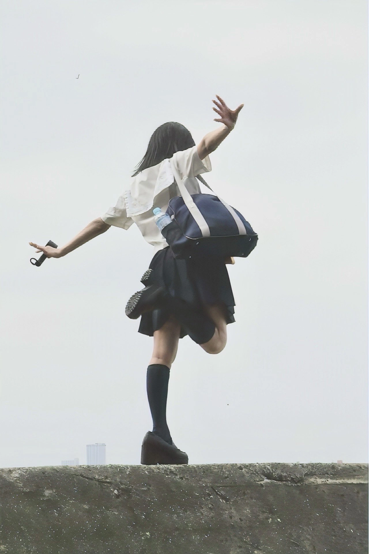 一位穿着白色衬衫和黑色衬衫的女人带着蓝色袋子在空中跳跃。