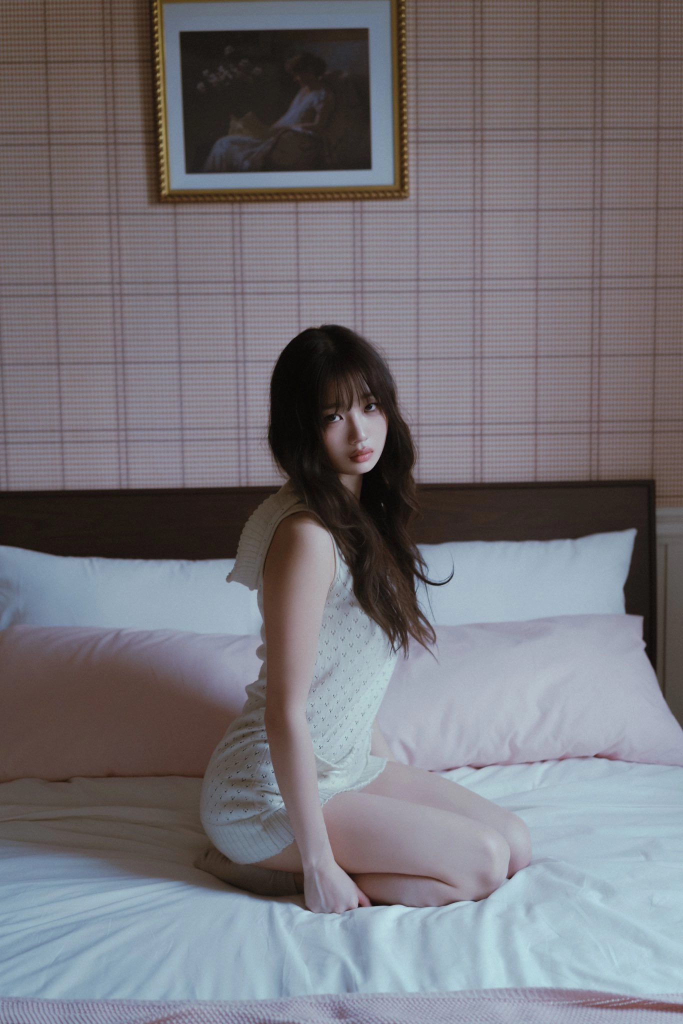 女人坐在床上,戴着粉红色的毯子。