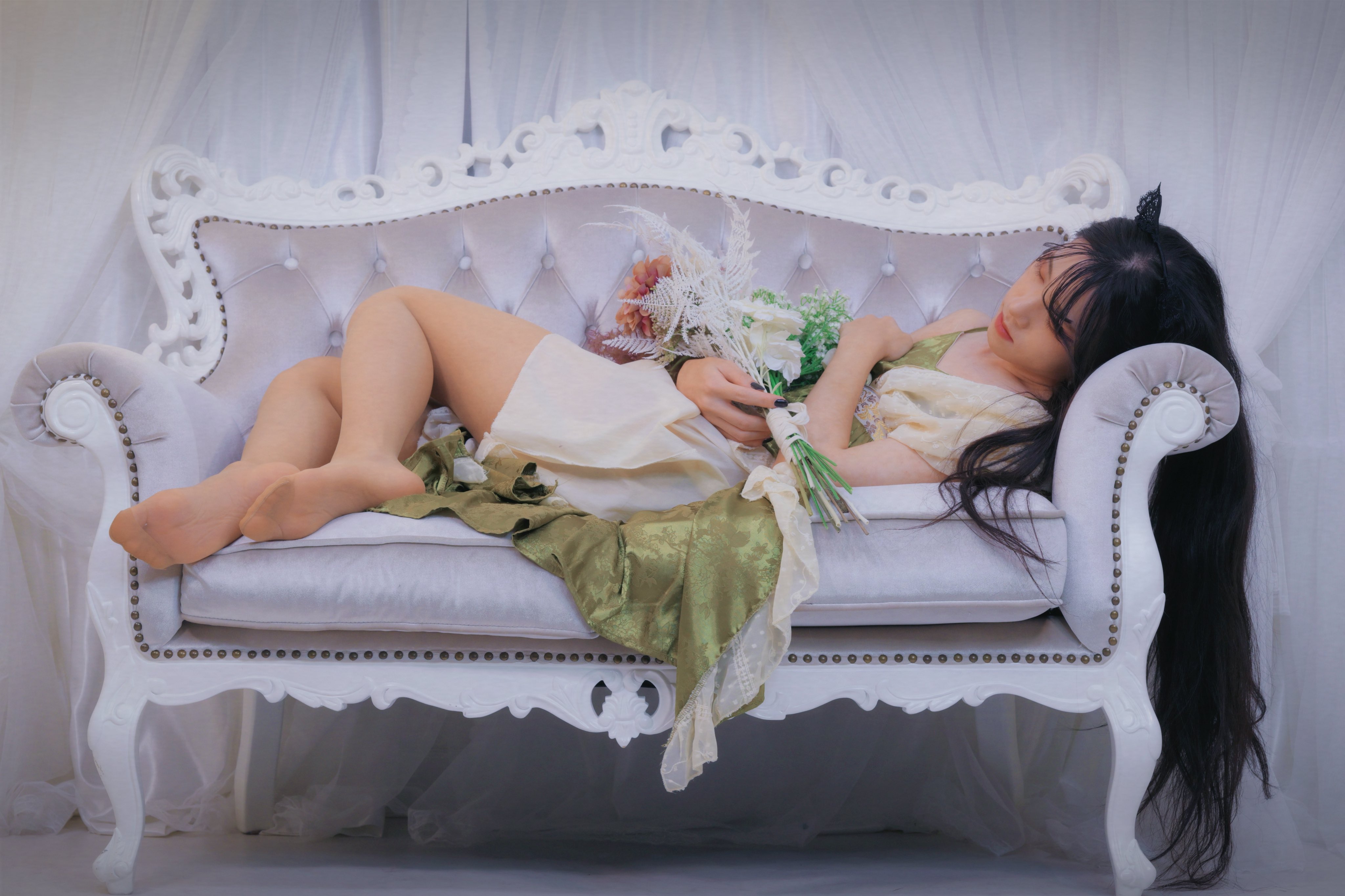 女人躺在一张白色的沙发上,手里拿着花。