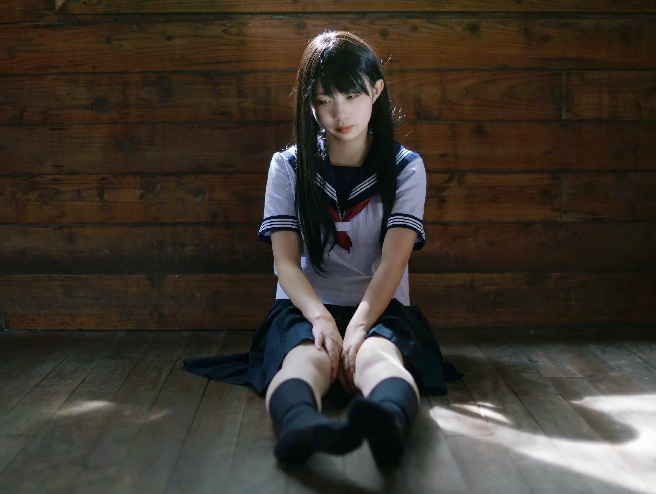 一位穿着白色衬衫和黑色裙子的女孩坐在木地板上。