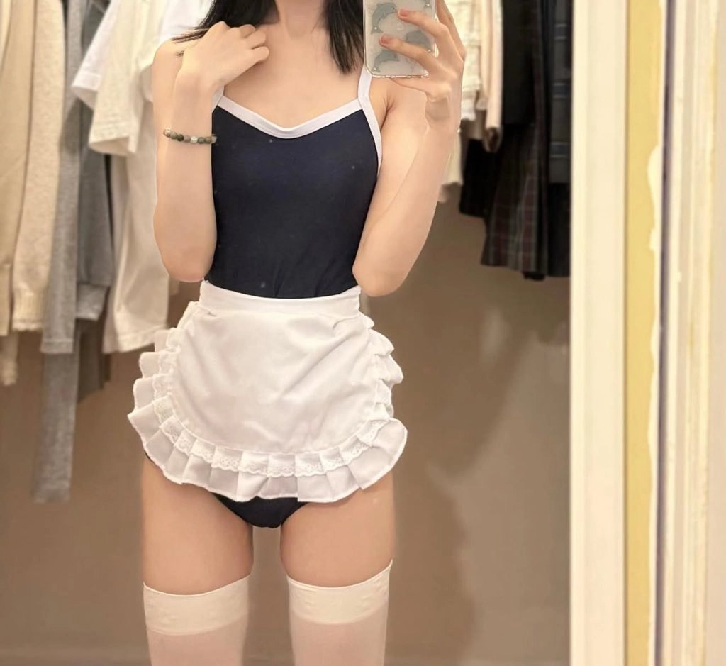 一位穿着蓝色裙子和白色外套的女人在镜子前拍自拍。