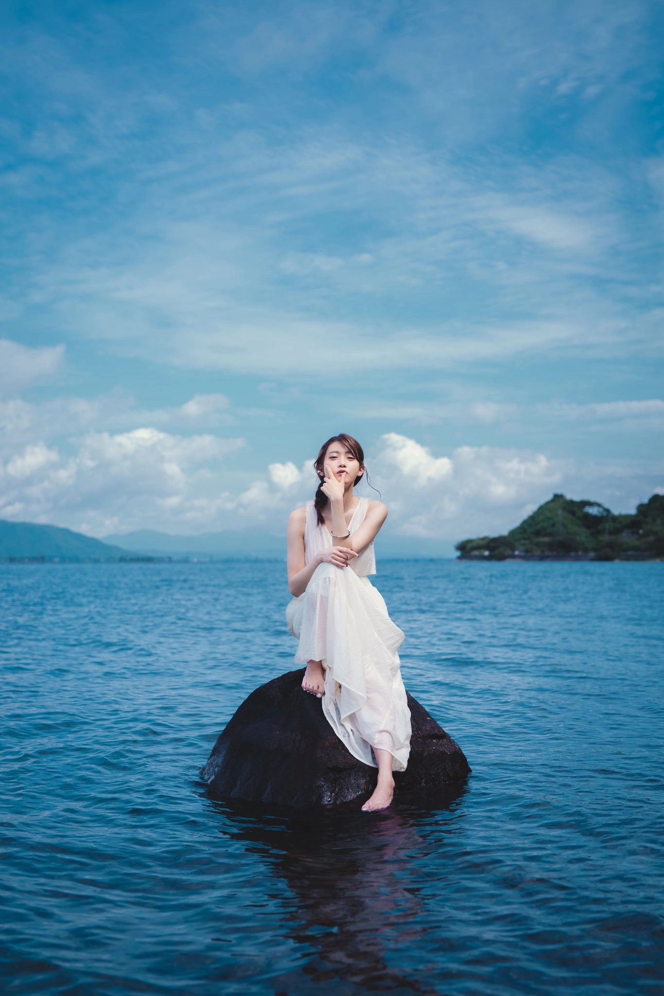 穿着白色衣服的女人坐在水中的岩石上。