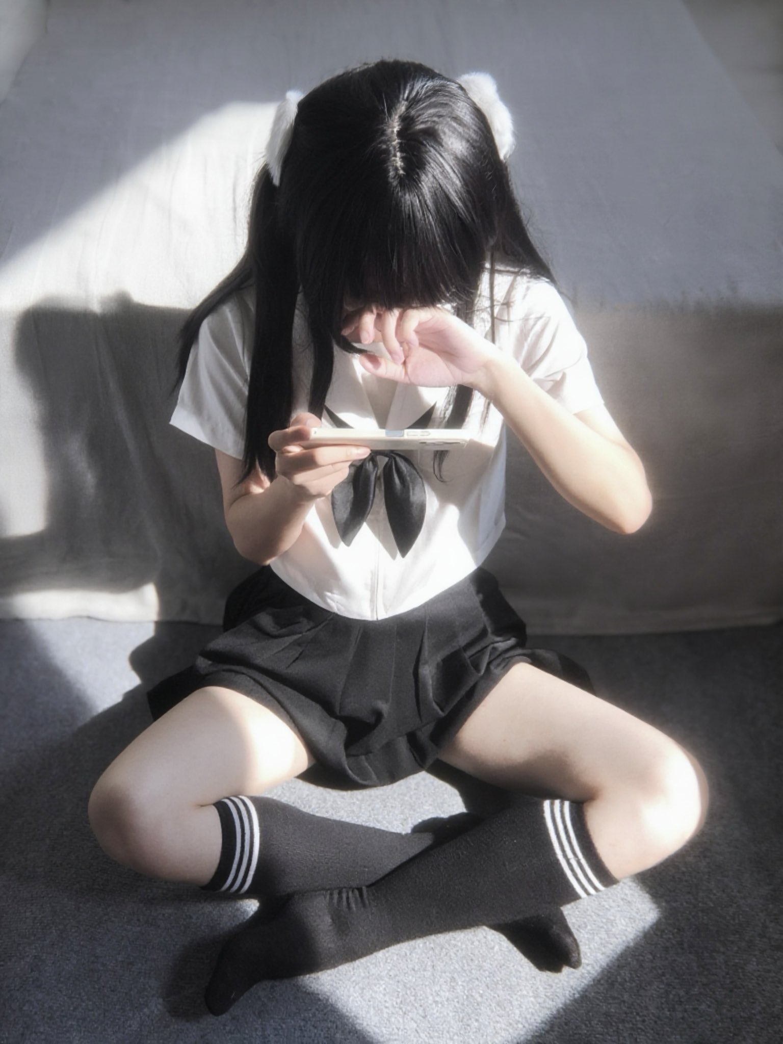 一位穿着白色衬衫和黑色裙子的女孩坐在地板上,看着她的手机。
