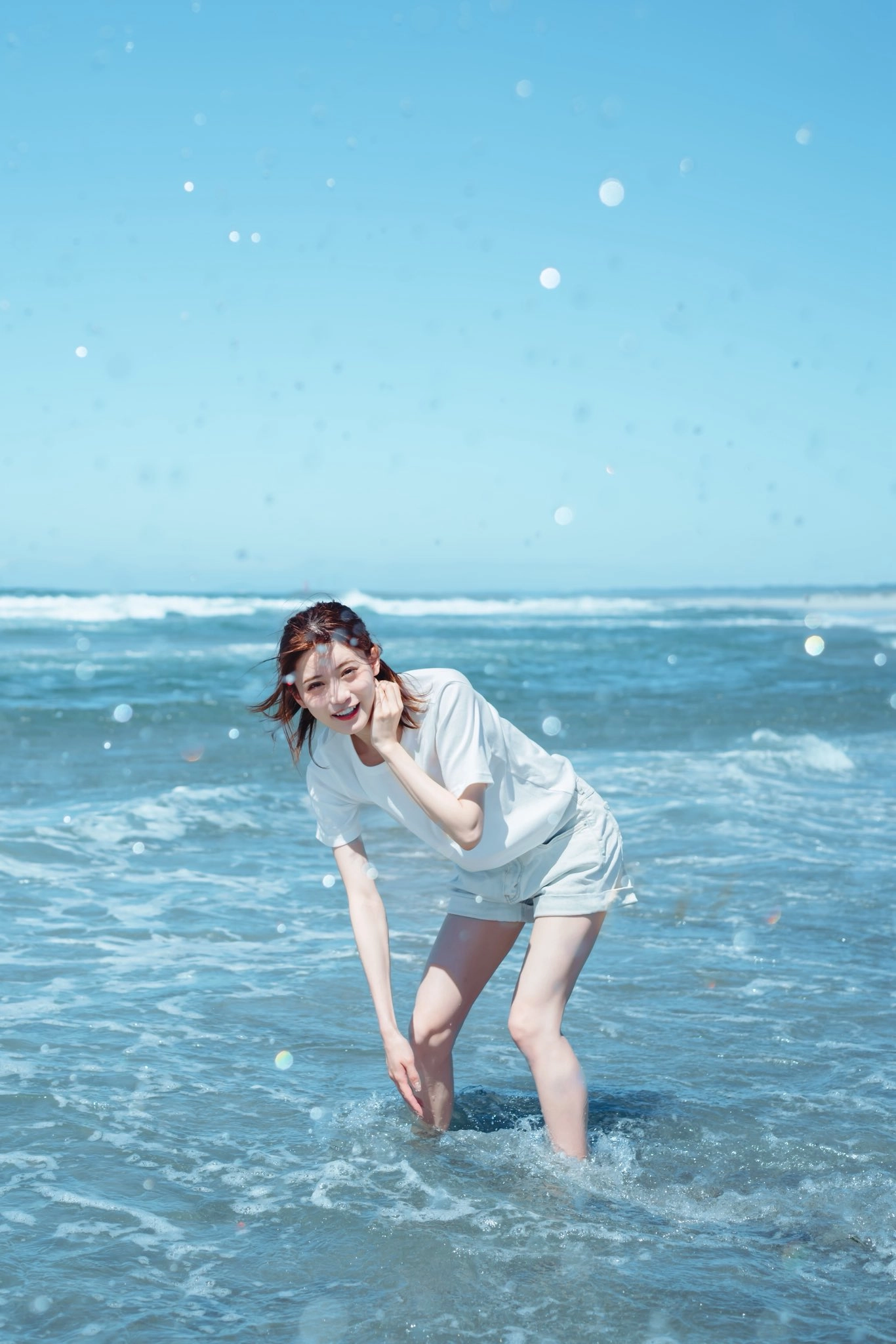 一位穿着白色衬衫和短裤的女人站在海里。