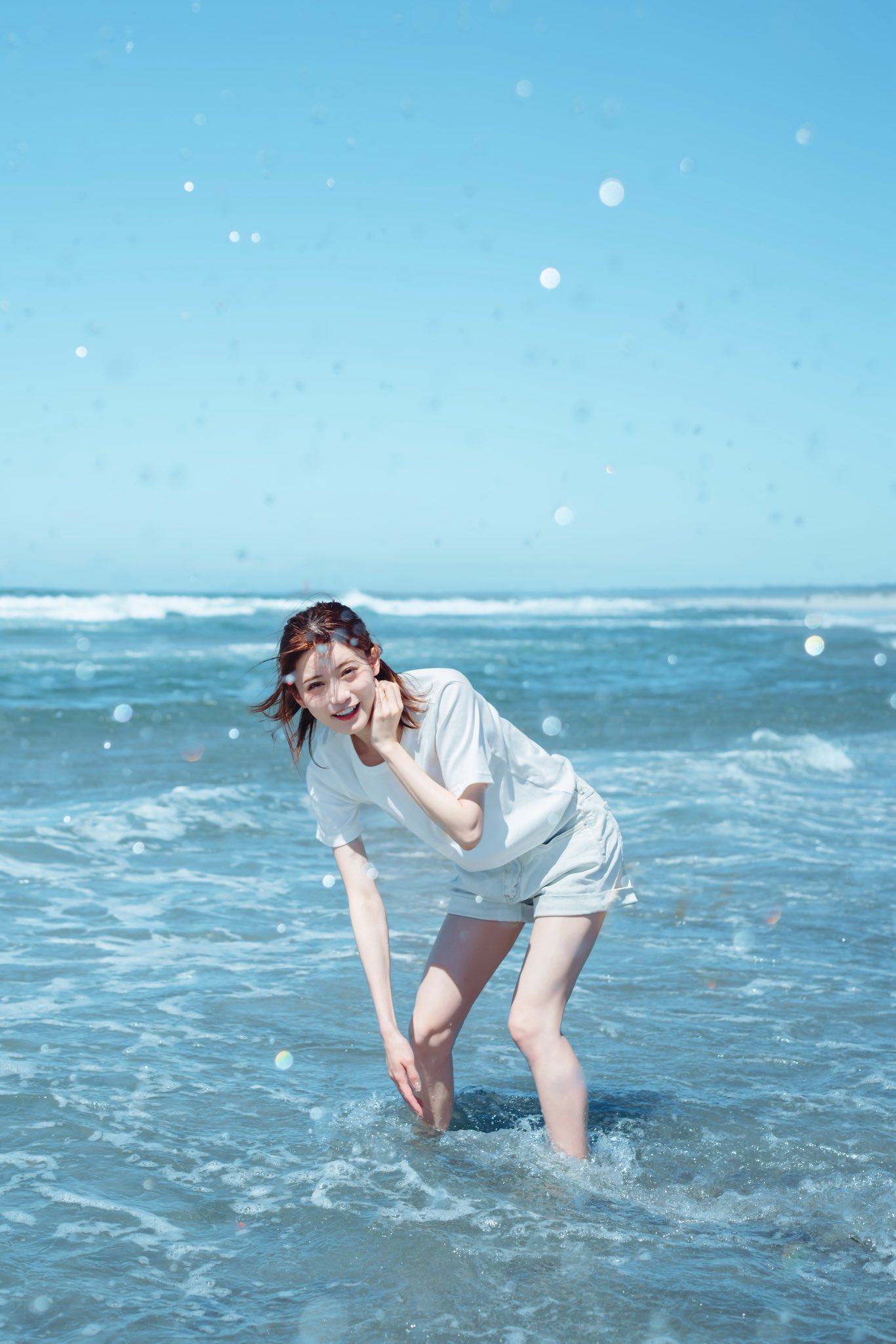 一位穿着白色衬衫和短裤的女人站在海里。