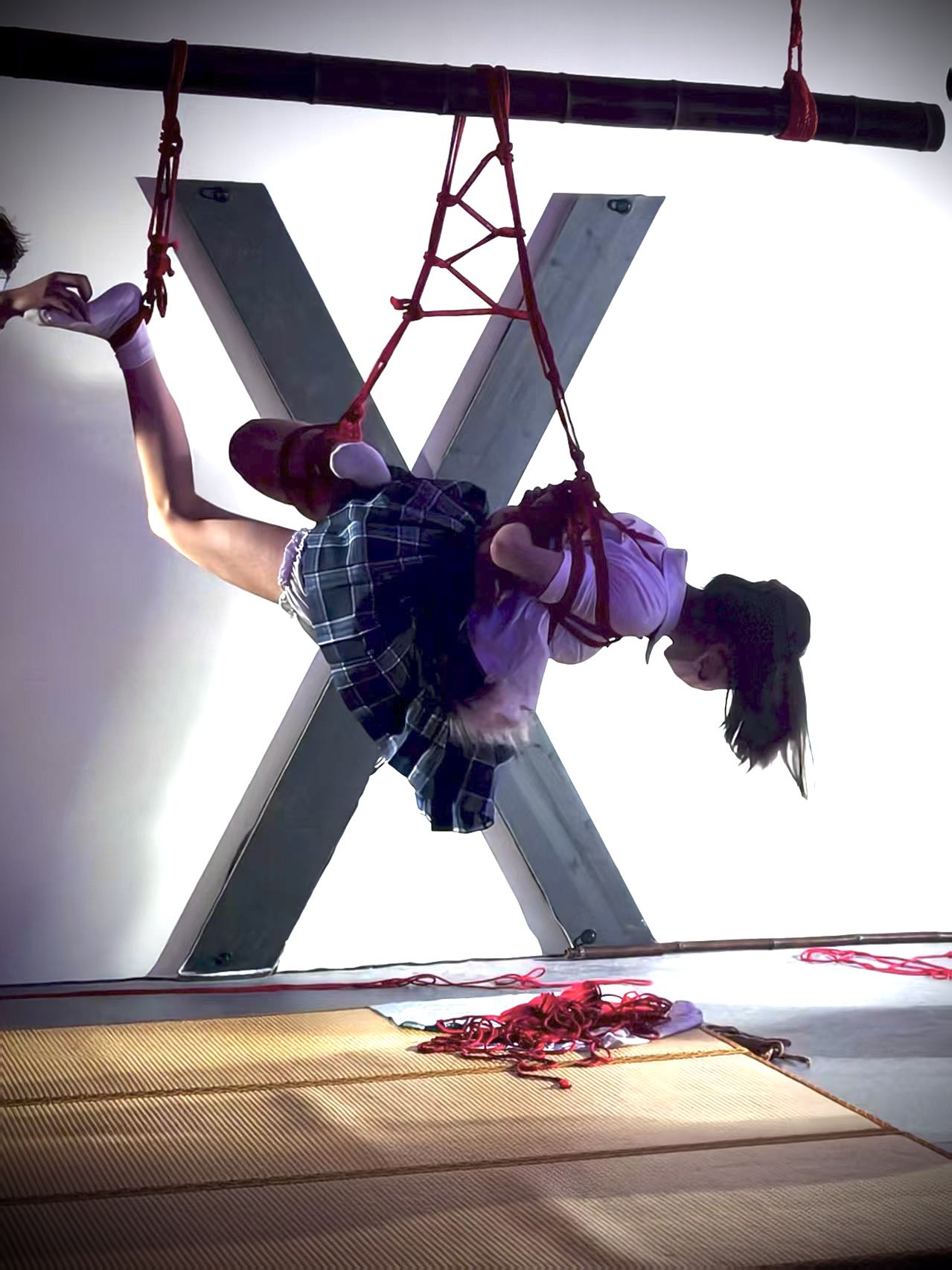 女人被绳子挂在一个大X前面。