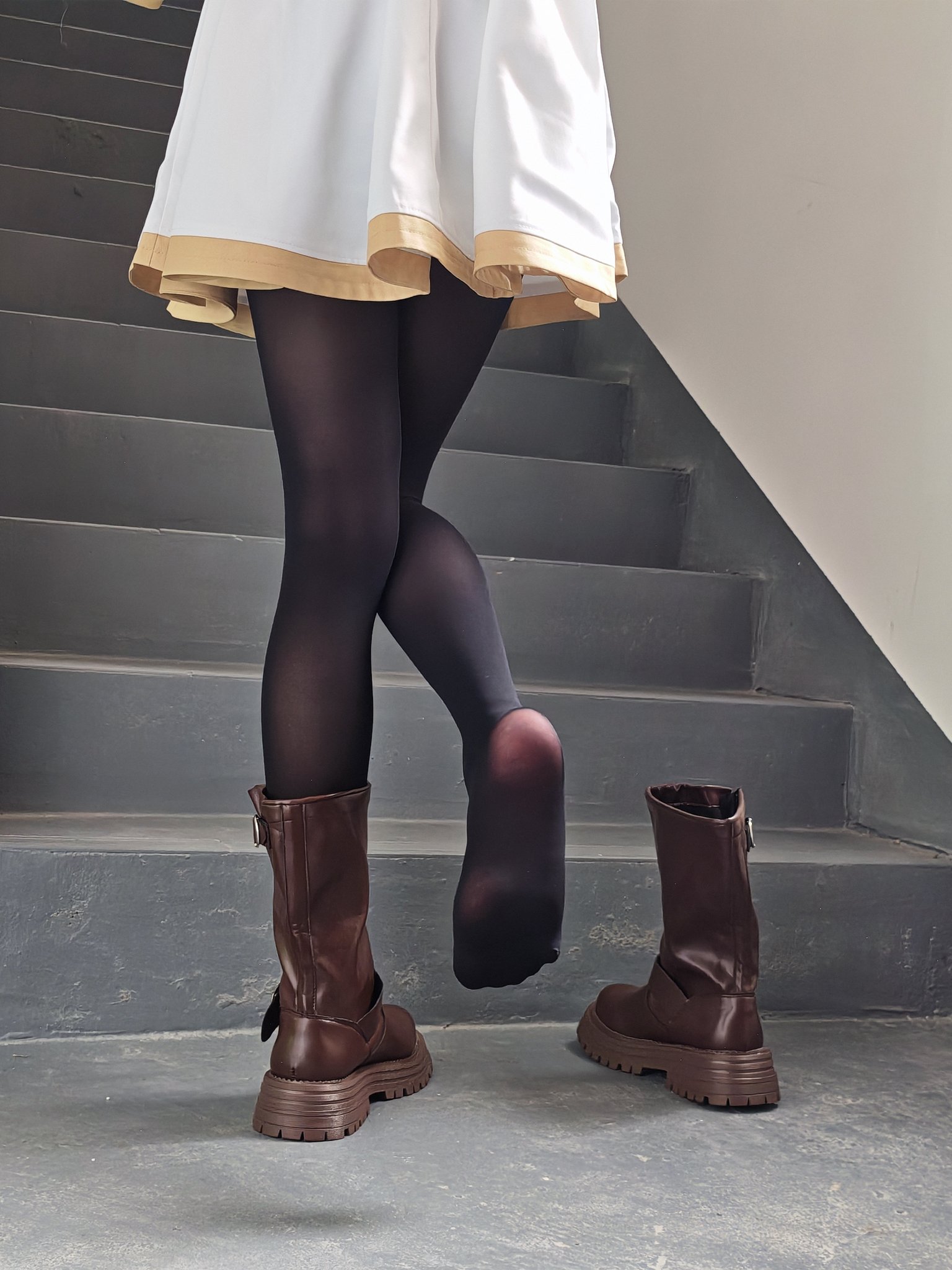 一位穿着黑色袜子和棕色靴子的女人站在楼梯上。