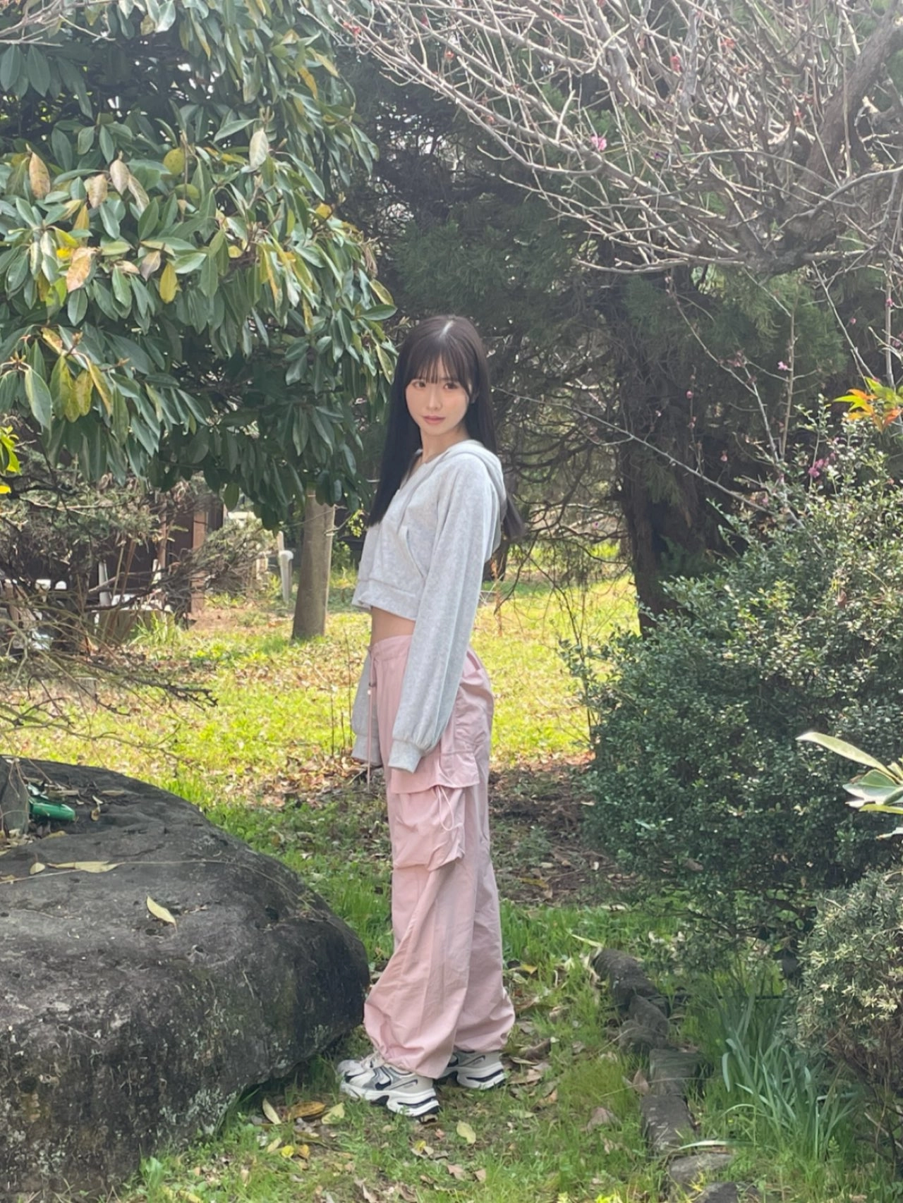 穿着灰色衬衫和粉红色的裤子的女人站在一棵树前。