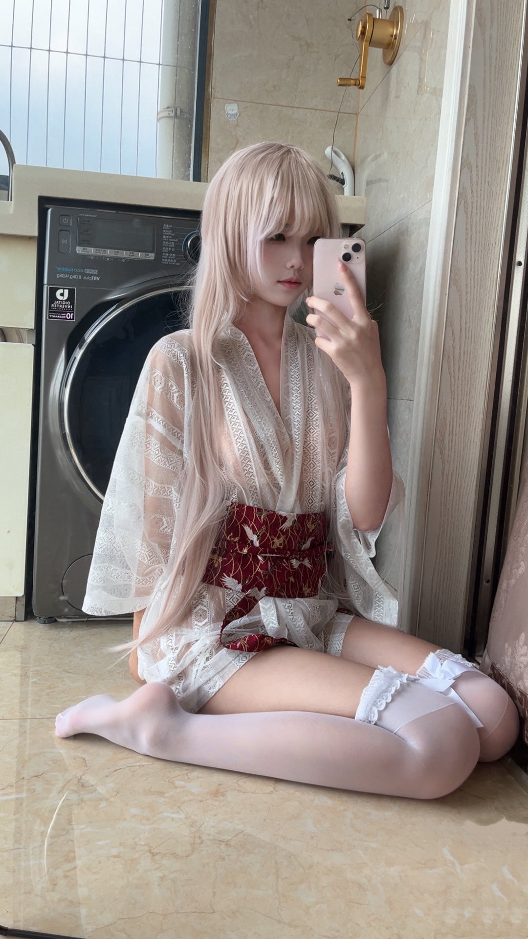 一位穿着白色裙子和红色带的女人在洗衣机前拍自拍。