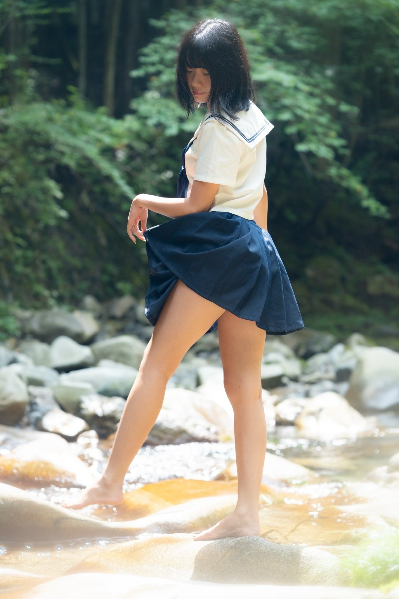 穿着蓝色裙子和白色衬衫的女人站在一条河流里。