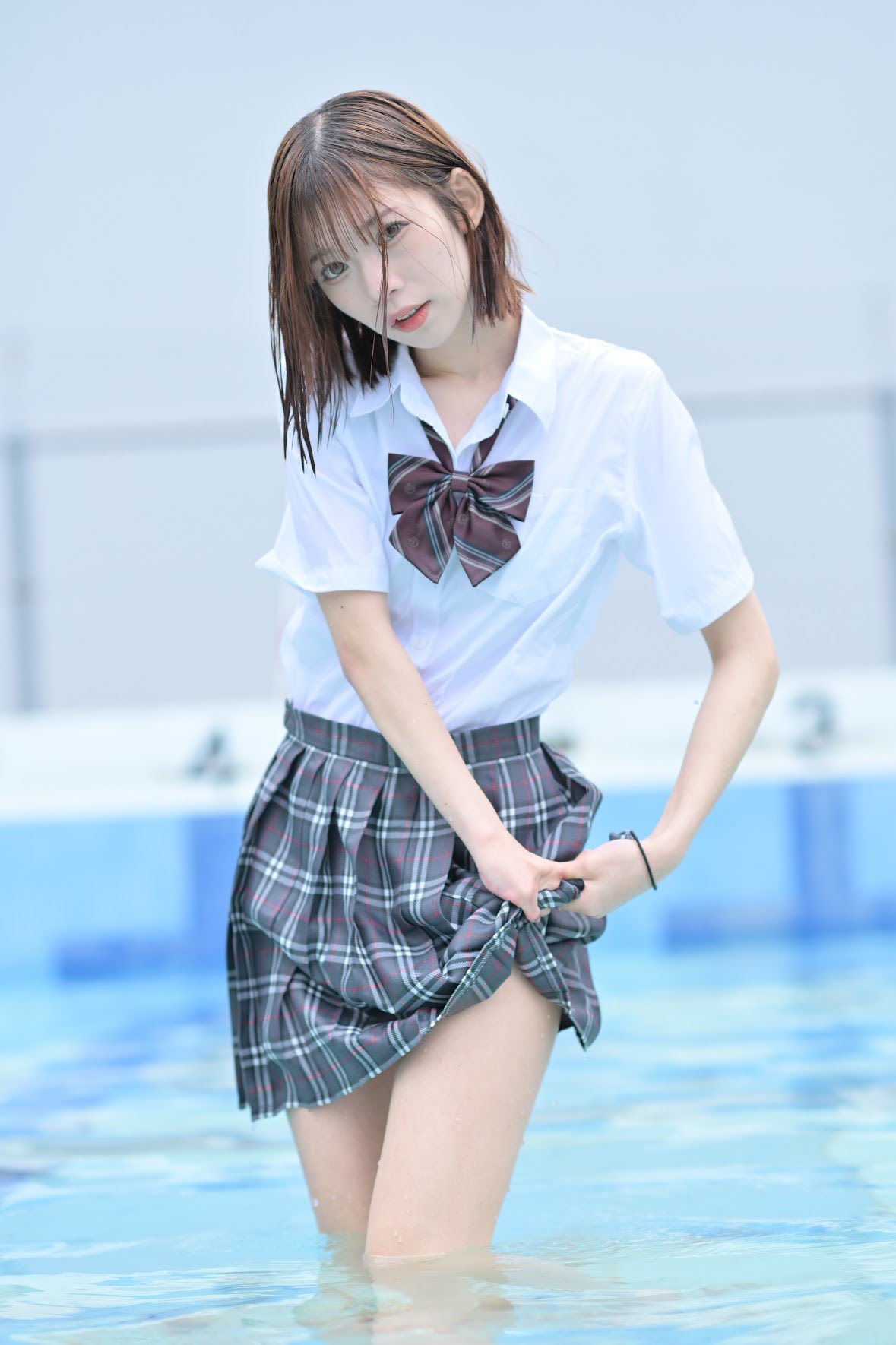 一位穿着白色衬衫和裙的女孩站在游泳池里。