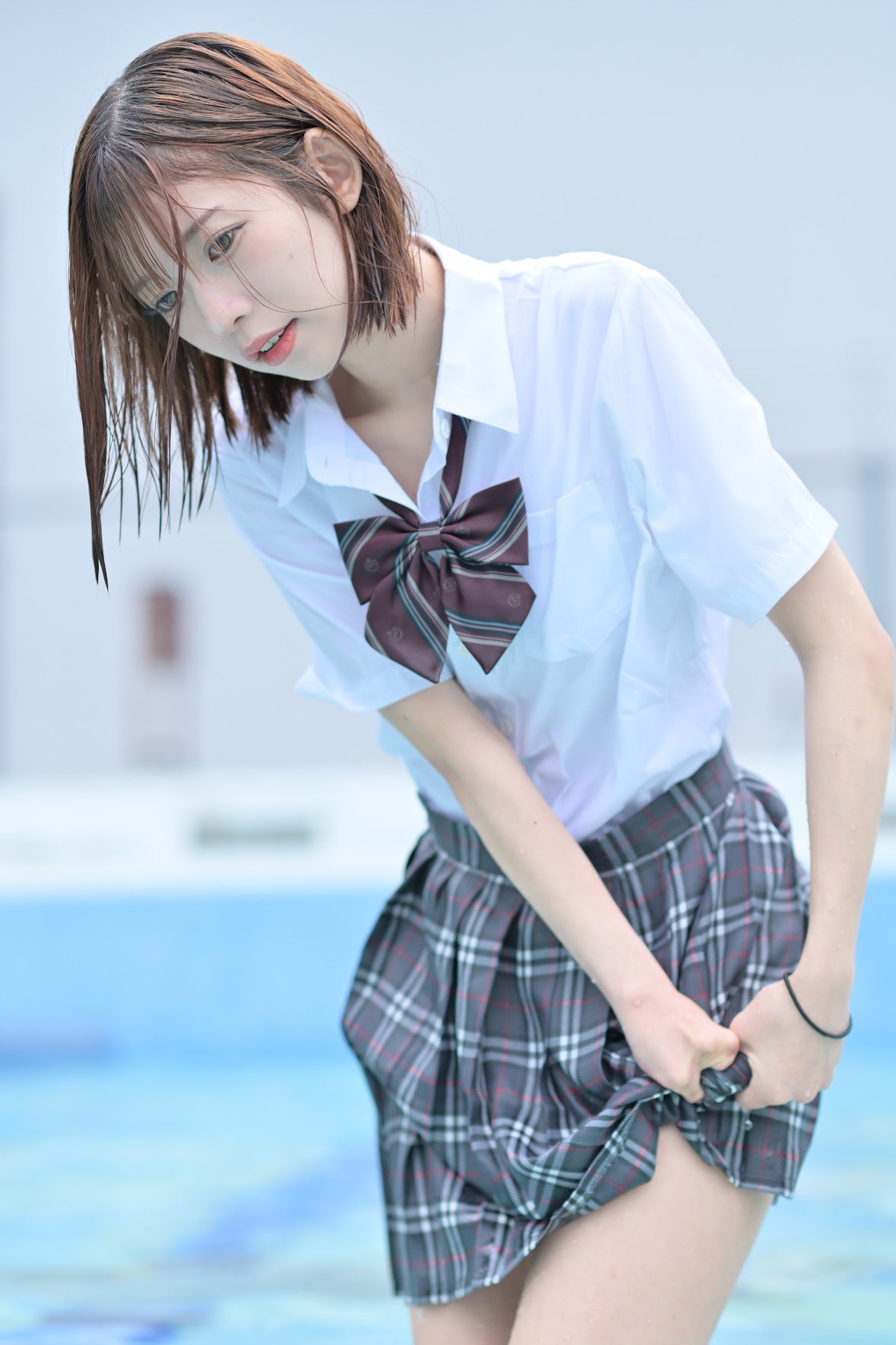 一位穿着白色衬衫和裙的女孩站在游泳池里。