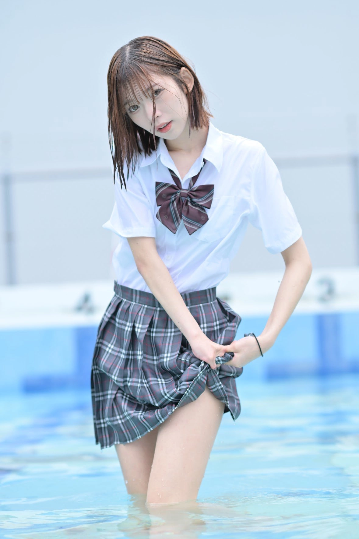 一位穿着白色衬衫和裙的女孩站在游泳池里。