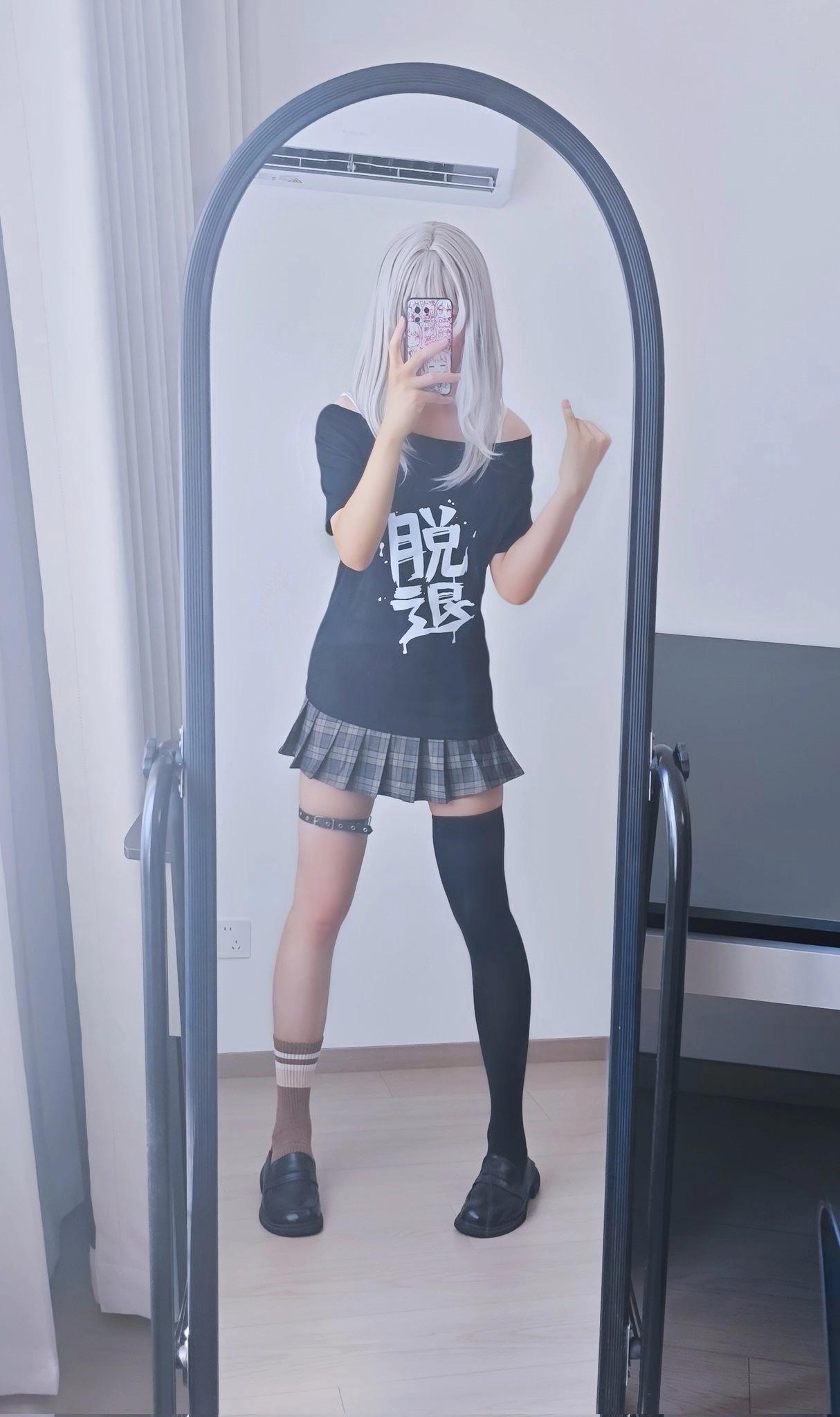 一位穿着黑色衬衫和裙子的女人在镜子前拍自拍。