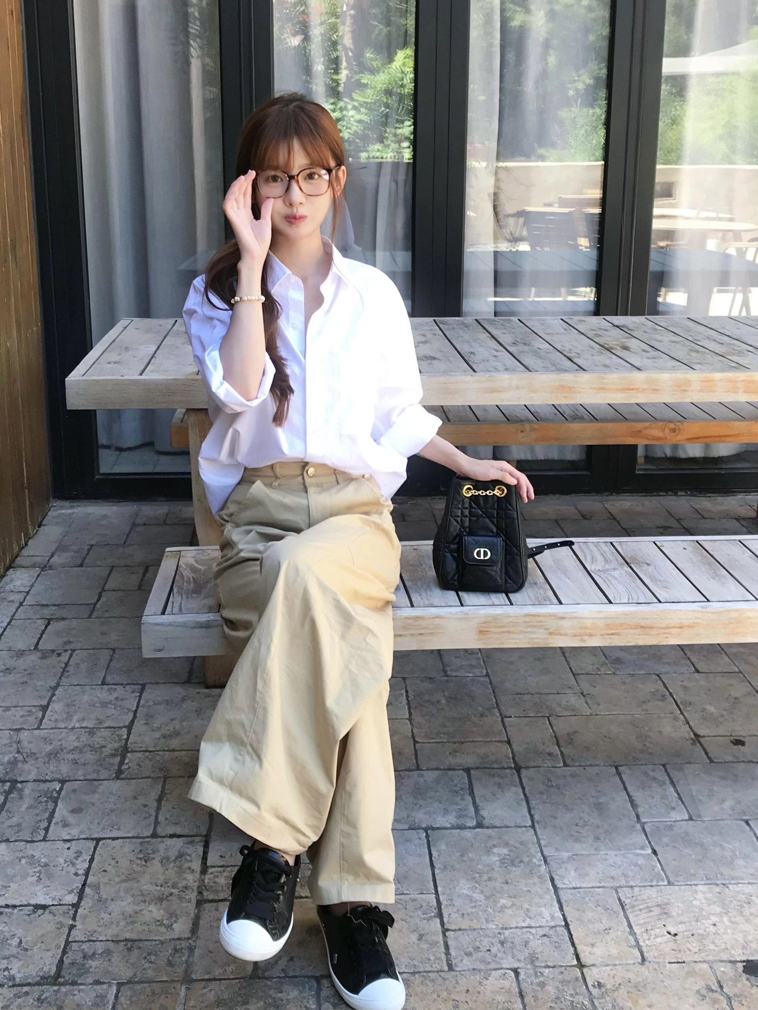 一位戴着眼镜和一件白色衬衫的女人坐在带钱包的凳子上。