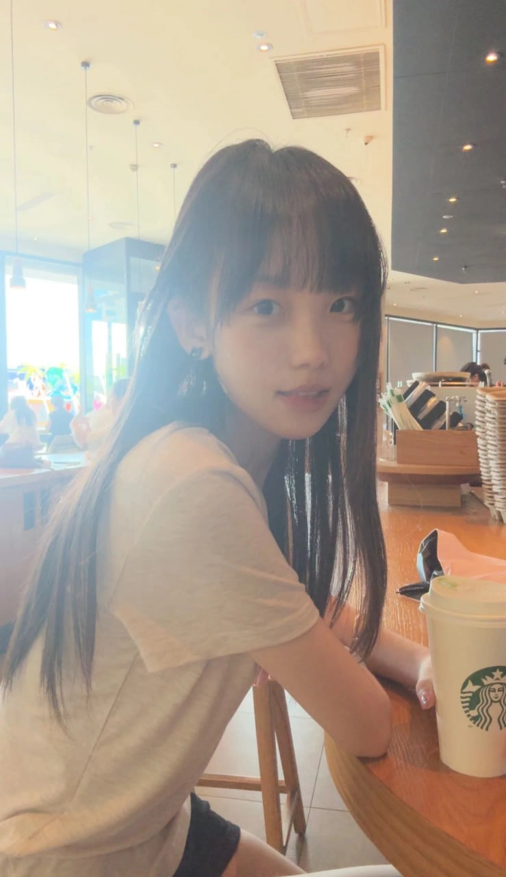 长头发和白衬衫的女人坐在一张带一杯咖啡的桌子上。