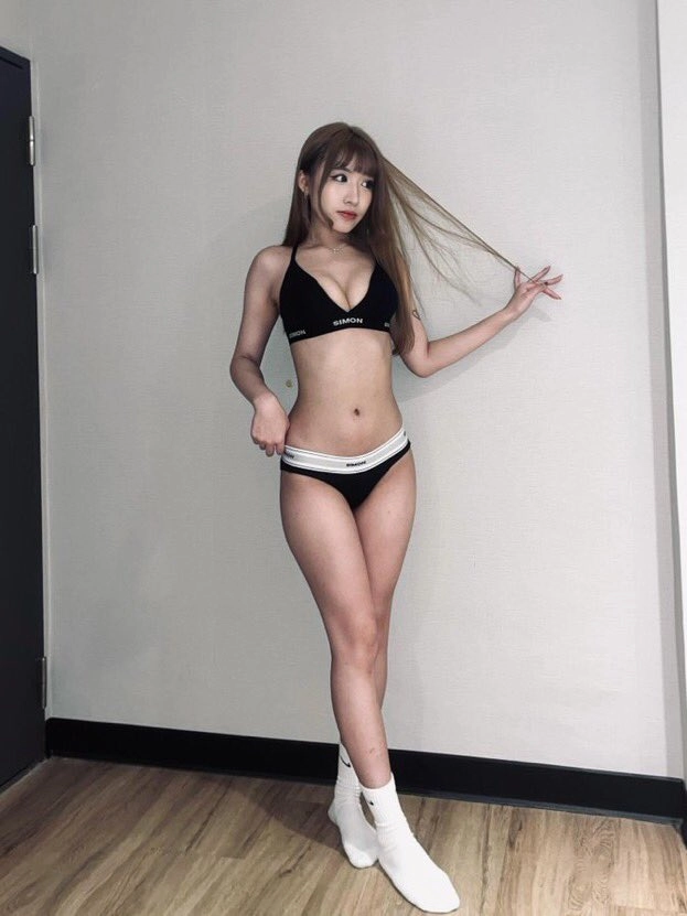 一位穿着黑色比基尼的女人站在一堵白色的墙前。