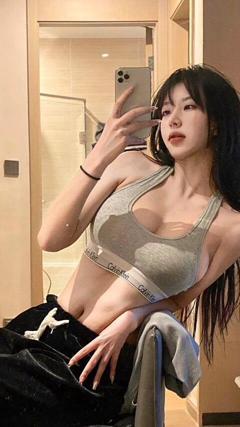 一位穿着灰色衬衫和黑裤子的女人在镜子前拍个自拍。